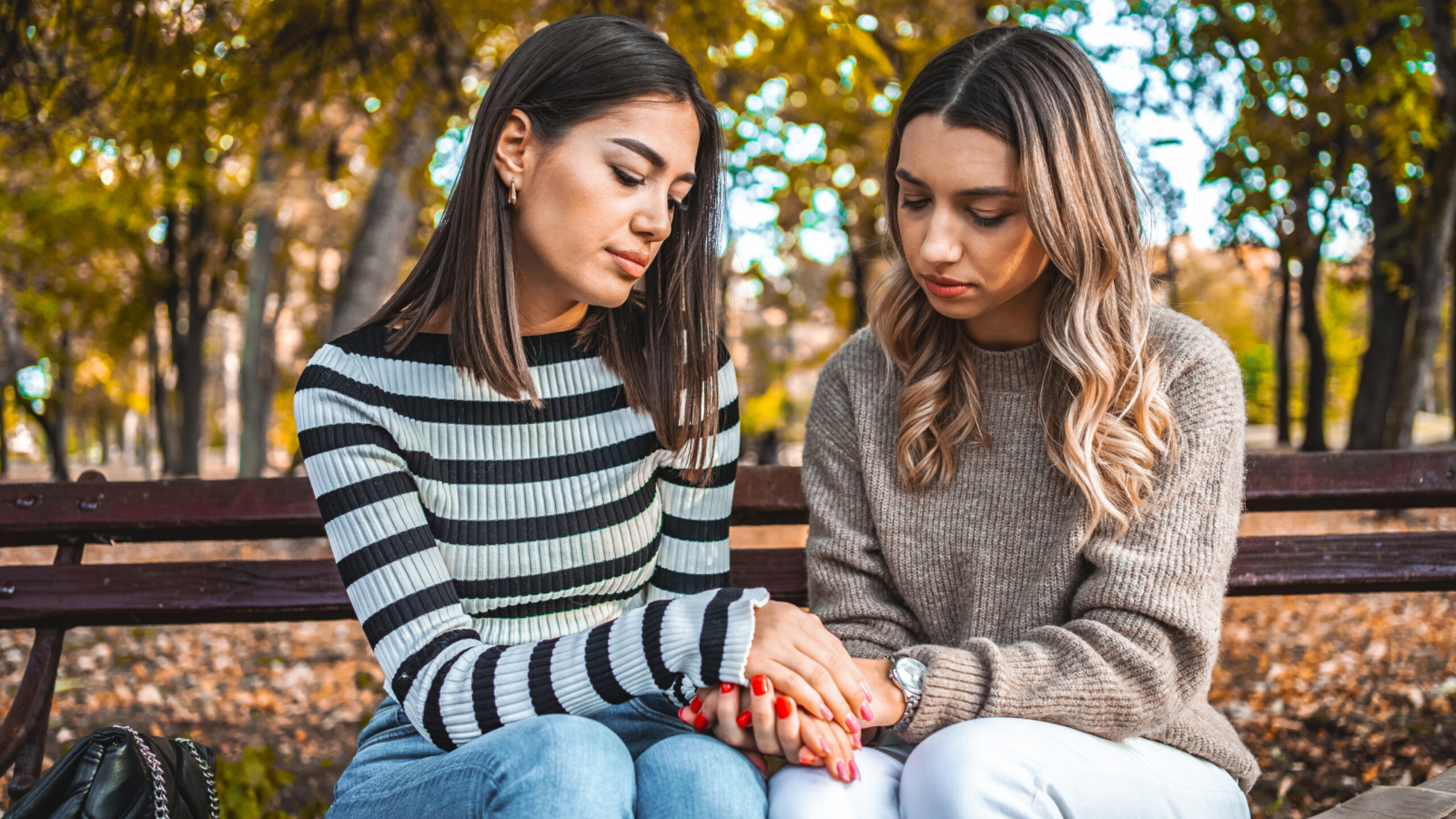 Young woman comforting her sad friend in the park during autumn